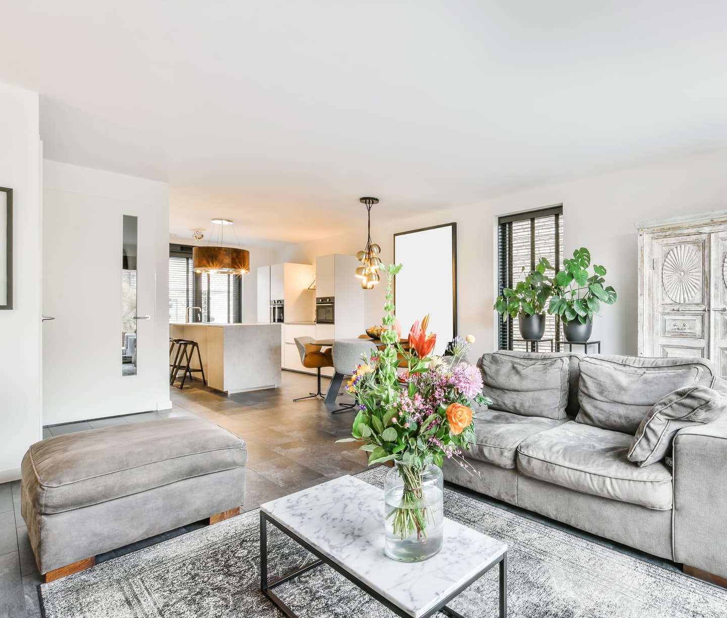 Bright living room with grey sofas and a vase of flowers, open to a modern kitchen and dining area