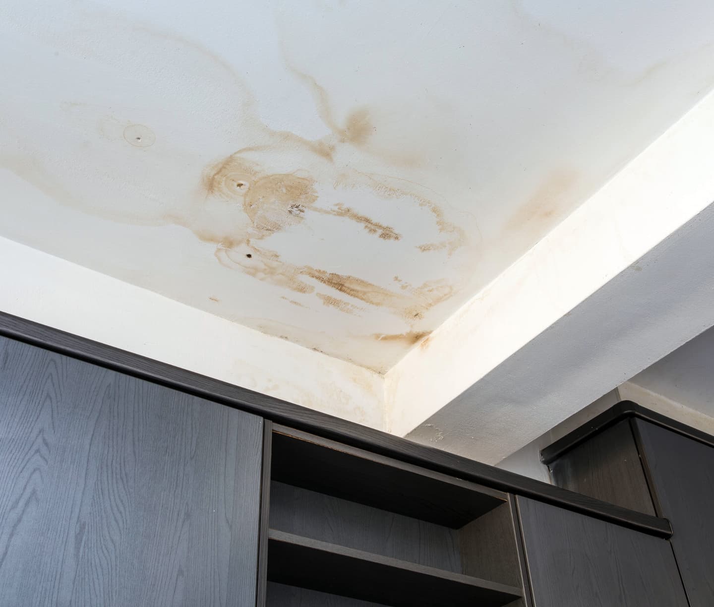 Brown water stains spreading across a white ceiling above dark wood cabinets